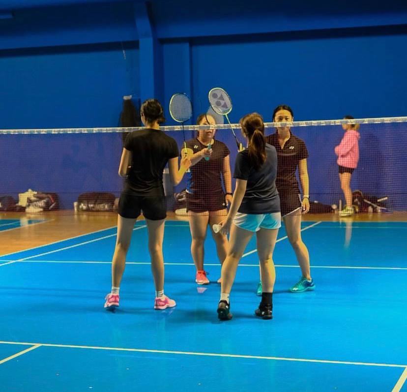 Coach guiding a badminton student through a practice drill on court